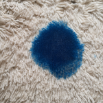 blue ink stain on the carpet – close-up of bright blue ink on a light rug