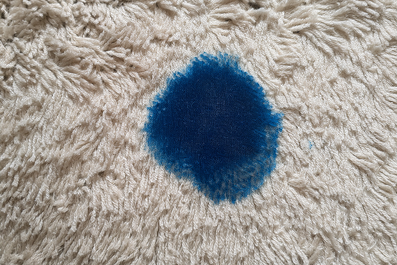 blue ink stain on the carpet – close-up of bright blue ink on a light rug