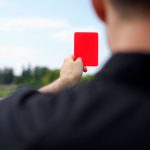 A red card held up on a soccer field, symbolizing sports fairness and controversy